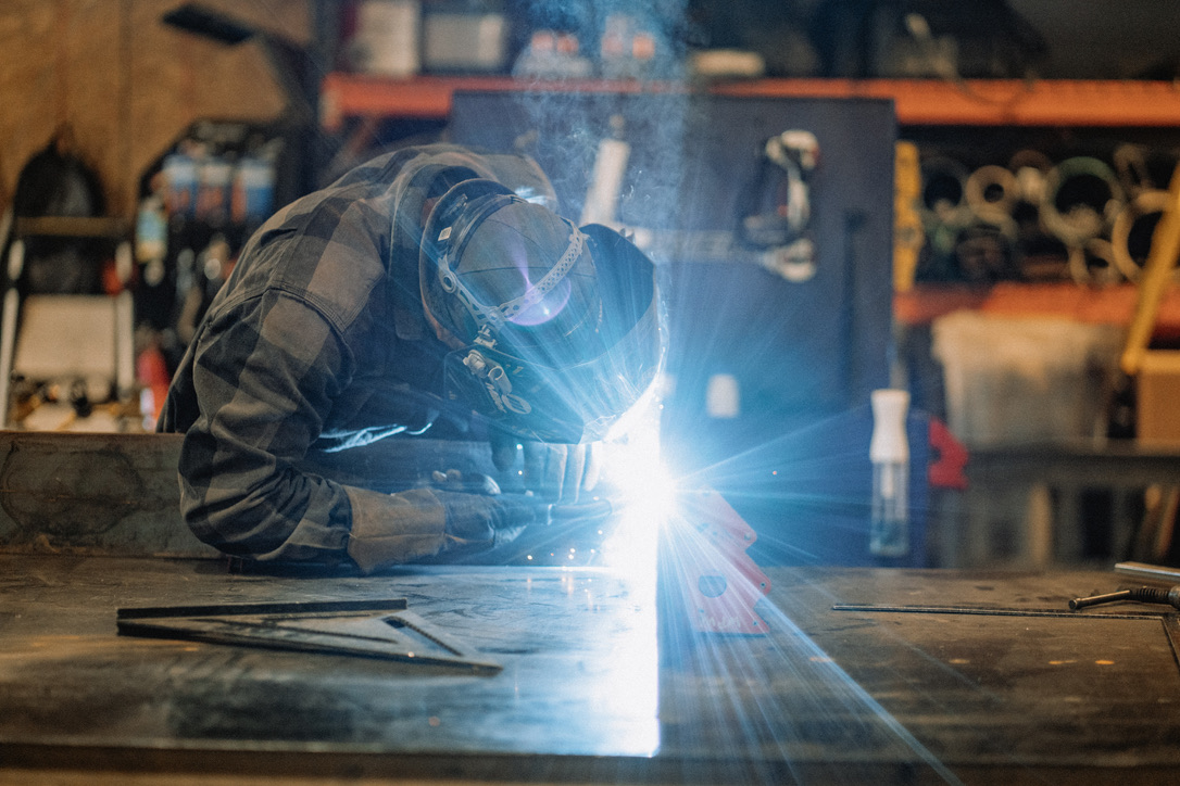 A craftsperson welding at a workbench, illuminated by blue light